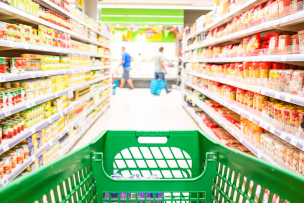 Nahaufnahme und erste Person oder Blick auf einen Einkaufswagen, der Produkte und Lebensmittel in einem leeren Supermarkt kauft - Menschen, die Lebensmittel auf einem Markt kaufen  - Foto, Bild