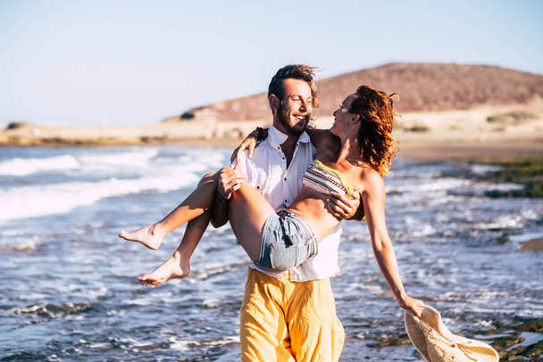 piękna para dwojga dorosłych na wakacjach i wakacjach bawiąc się razem - mężczyzna niosący kobietę z miłością na plaży   - Zdjęcie, obraz