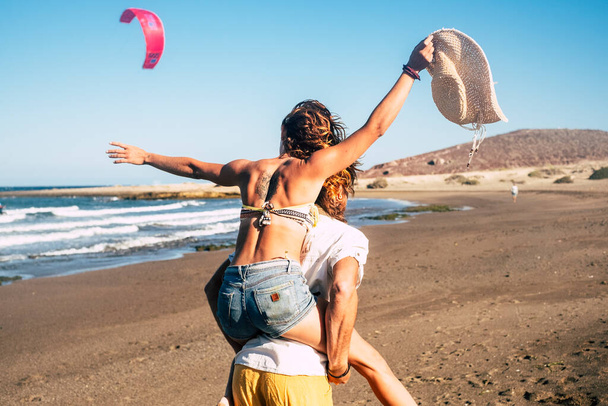 couple of beautiful adults get engaged and married together at the beach - woman on the shoulders of the man looking at him and smiling  - Photo, Image