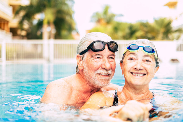 pareja de dos ancianos abrazados en el agua de la piscina - hombre y mujer activos haciendo ejercicio juntos en la piscina - abrazados con amor  - Foto, Imagen