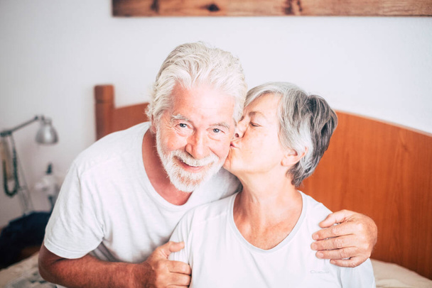 couple of seniors looking  and smiling with love and affect while she's kissing he - retired and mature adults married at the bedroom at the morning before get up  - 写真・画像