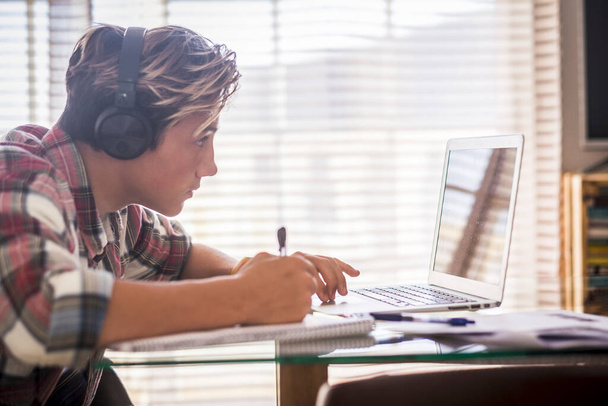 Close up de adolescente com fones de ouvido olhando para a tela do laptop durante a reprodução de jogos de computador, conversando na Internet ou vendo vídeos - Foto, Imagem