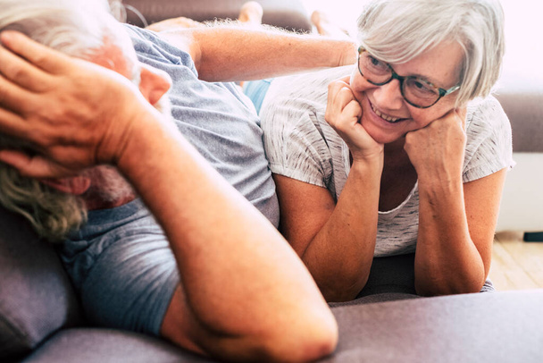 coppia di due anziani in relazioni e sposati sdraiati sul divano insieme - donna che guarda l'uomo sorridente - amore e affetto   - Foto, immagini
