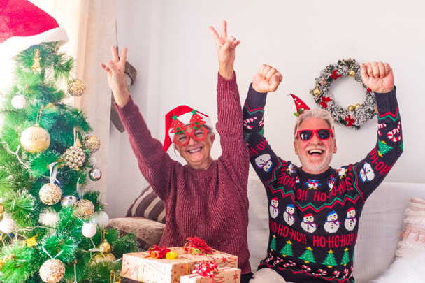 δύο τρελοί και αστείοι ηλικιωμένοι που παίζουν διασκεδάζοντας μαζί και γιορτάζοντας να κάνουν ένα πάρτι στο σπίτι την ημέρα των Χριστουγέννων πριν τυλίξουν τα δώρα και τα δώρα  - Φωτογραφία, εικόνα