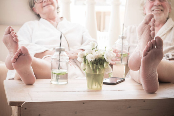 dva důchodci nebo senioři sedící v interiéru v resortu nebo hotelu na kosmetické proceduře - zblízka nohy na stole s koktejly  - Fotografie, Obrázek