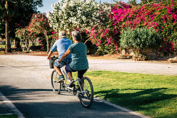 hermosa pareja de mayores y maduros casados, montando una bici doble, tándem, juntos para divertirse con un gran y soleado día - mujer y hombre  - Foto, Imagen