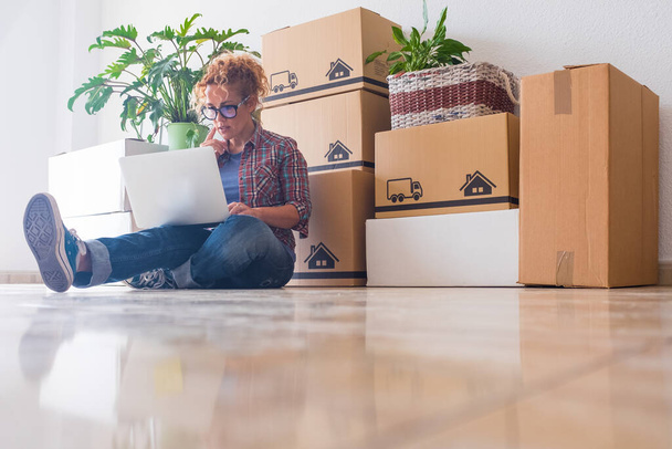 One young woman and happy people after buy a new house or apartment together to live together - person on the ground using laptop with boxes ad packs on her back  - Photo, Image