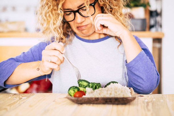 woman looking with disgust at some vegetables and rise on the table - she's not going to eat this because she prefer bad nutrition - trying losing weight  - Photo, Image