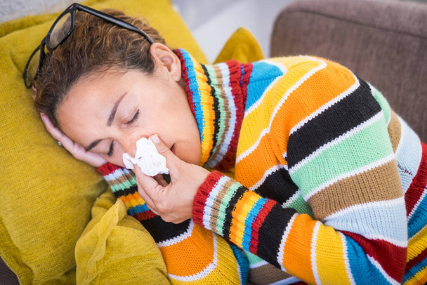 beautiful woman sitting at home on the sofa - tired woman with fever feeling upset with a napkin in her hand - woman feeling cold at winter indoor  - Photo, Image