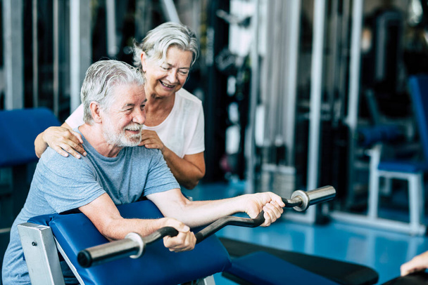 ζευγάρι ηλικιωμένων και ώριμων ανθρώπων που εκπαιδεύονται μαζί στο γυμναστήριο για να εκπαιδεύσουν τα σώματά τους - γυναίκα που βοηθά τον ενήλικο άνδρα να κάνει άσκηση   - Φωτογραφία, εικόνα