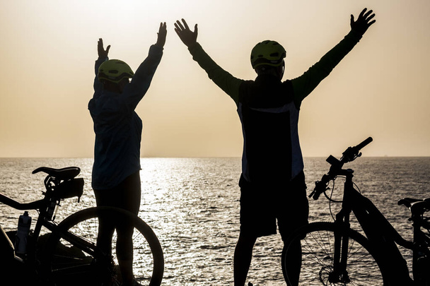 krásné siluety páru seniorů na pláži s koly a s rukama nad hlavou - vítězové a úspěšný koncept životního stylu  - Fotografie, Obrázek