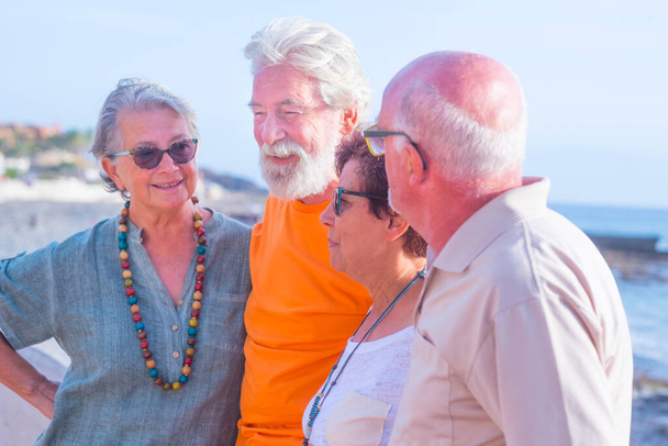 grupo de cuatro personas mayores felices y personas maduras hablando y divirtiéndose juntos en la playa con el mar en el fondo - concepto de amistad y relación  - Foto, imagen