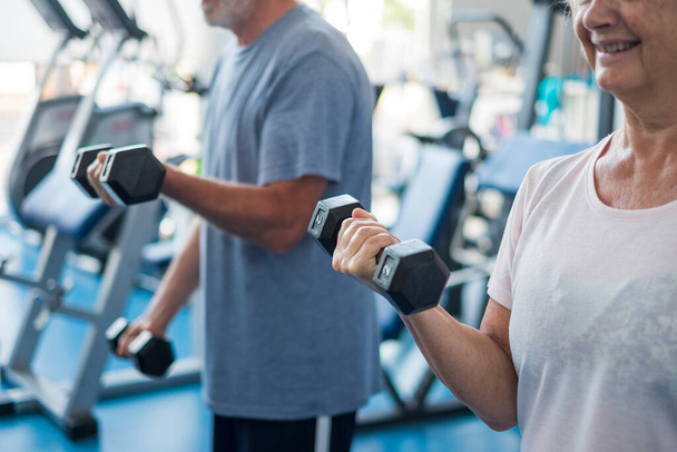 pareja de dos personas mayores y personas maduras en el gimnasio haciendo ejercicio adultos sosteniendo una mancuerna y trabajando bíceps juntos  - Foto, Imagen