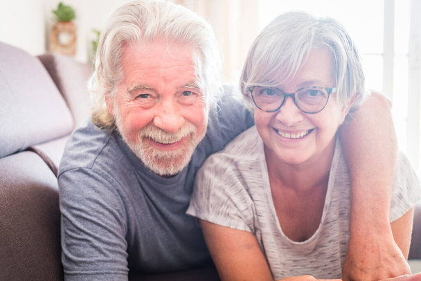 coppia di due anziani e persone mature sdraiate sul divano a guardare la telecamera sorridente e ridente - sposati con vivere per sempre a casa  - Foto, immagini