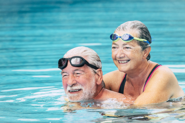 para seniorów przytulona w wodzie basenu - aktywny mężczyzna i kobieta ćwiczący razem na basenie - przytuleni z miłością - noszący gogle  - Zdjęcie, obraz