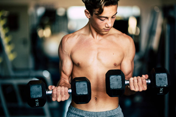 egy tinédzser egyedül az edzőteremben edzés és emelés súlyzók - erős és izmos ember - fitness és izom életmód  - Fotó, kép