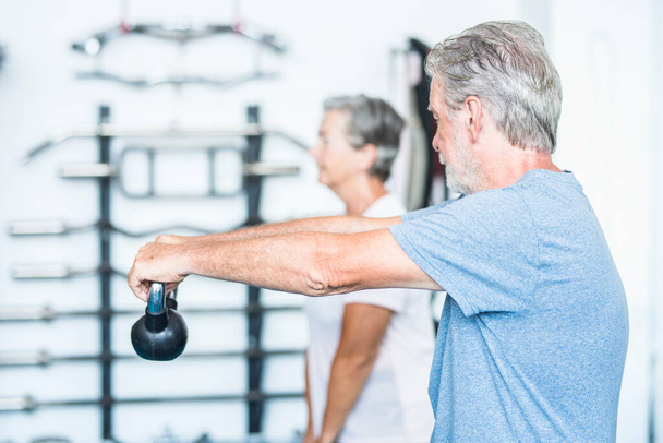 deux personnes âgées travaillant sur son corps pour être en bonne santé ensemble à la salle de gym tenant un poids - couple de personnes matures de formation   - Photo, image