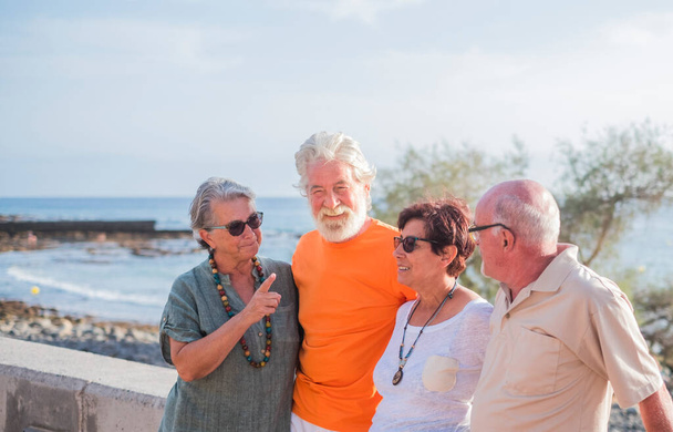 group of seniors and mature people at the beach taking together and having fun with the sea or the ocean at the background - four persons - Photo, Image