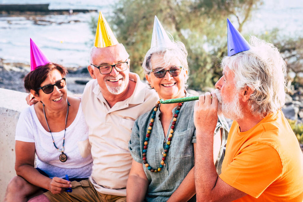 groupe de personnes âgées et matures assis à la plage avec la casquette de la fête et à la recherche d'un homme et rire - fête ou concept d'anniversaire  - Photo, image