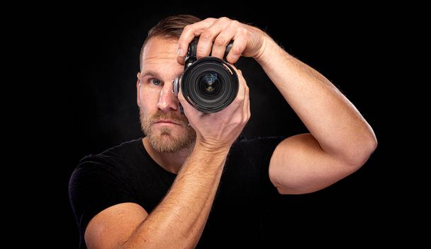 Un homme barbu prend des photos avec un appareil photo sur un fond sombre. - Photo, image