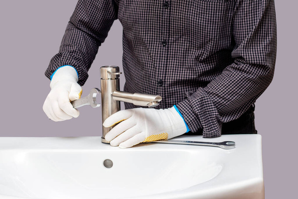 Un plombier avec une clé à la main installe un robinet sur un évier - Photo, image