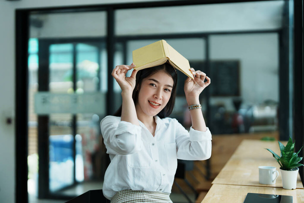 Portrait of a beautiful Asian female employee reading a book during her lunch break. - 写真・画像