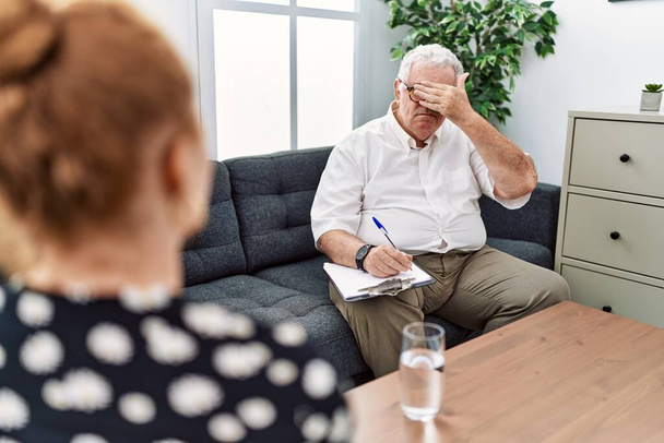Psicologo anziano all'ufficio di consultazione che copre gli occhi con la mano, sembra serio e triste. concetto di avvistamento, nascondiglio e rifiuto  - Foto, immagini