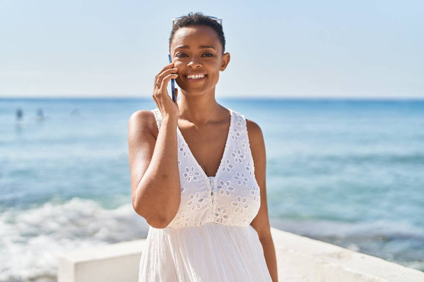Afro-Amerikan kadın gülümsüyor. Deniz kenarında akıllı telefondan konuşuyor. - Fotoğraf, Görsel