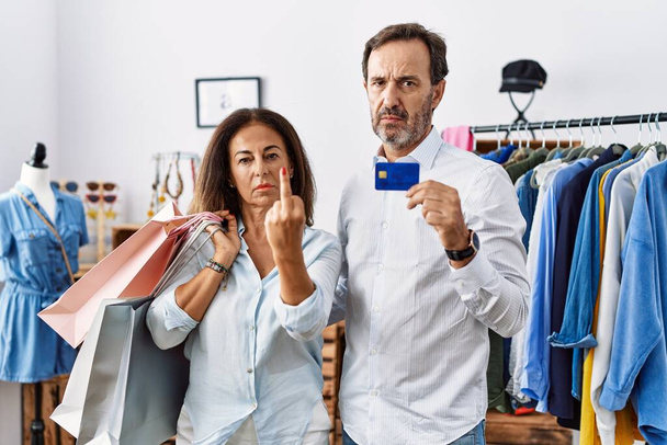 Hispanic middle age couple holding shopping bags and credit card showing middle finger, impolite and rude fuck off expression  - Photo, image