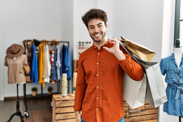 Young hispanic customer man smiling happy holding shopping bags at clothing store. - Foto, imagen