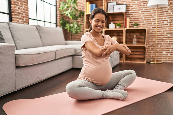jong latin vrouw zwanger glimlachen zelfverzekerd stretching thuis - Foto, afbeelding