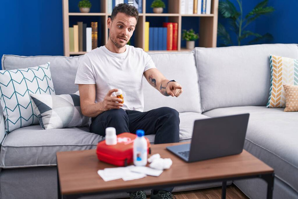 Young hispanic man watching video on laptop on how to use first aid kit pointing with finger to the camera and to you, confident gesture looking serious  - Photo, Image