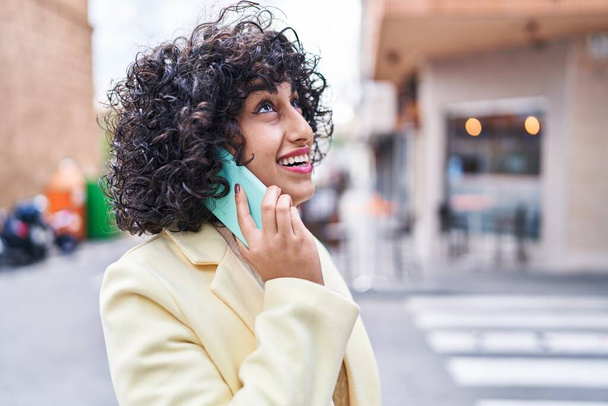 Jeune femme du Moyen-Orient excutive souriant confiant parler sur le smartphone à la rue - Photo, image