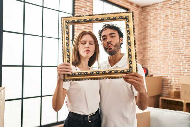 Young two people holding empty frame together making fish face with mouth and squinting eyes, crazy and comical.  - 写真・画像