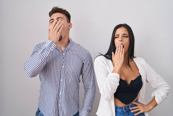 Young hispanic couple standing over white background bored yawning tired covering mouth with hand. restless and sleepiness.  - Photo, Image