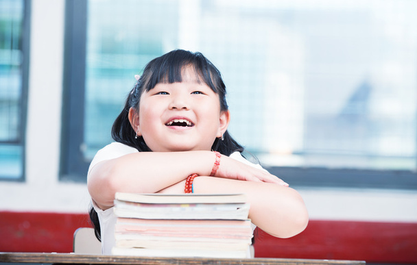 Porträt eines süßen asiatischen Mädchens auf einem Bücherstapel - Foto, Bild