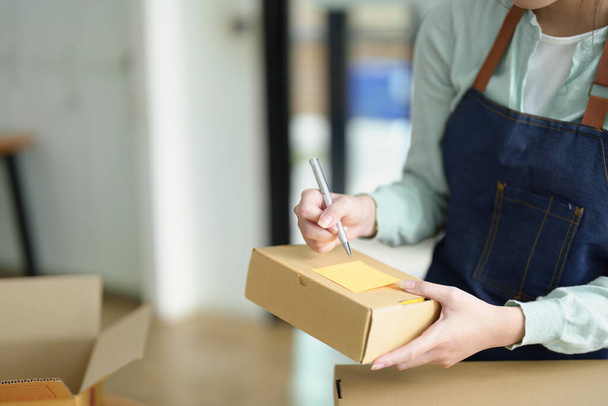 small startup, and SME owner, an Asian female entrepreneur, is writing down information on a notepad to organize the product before packing it into the inner box for the customer. - Valokuva, kuva