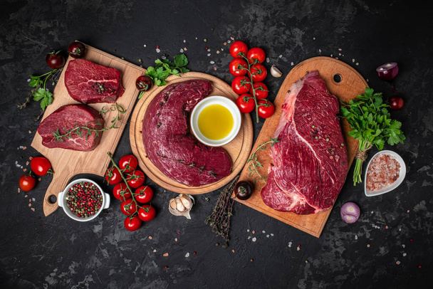 Fresh and raw beef meat. Whole piece of tenderloin with steaks and spices ready to cook on dark background, banner, menu, recipe place for text, top view, - 写真・画像