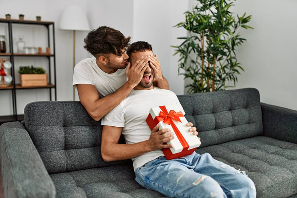 Two hispanic men couple surprise with gift and hands on eyes at home - Foto, Imagen