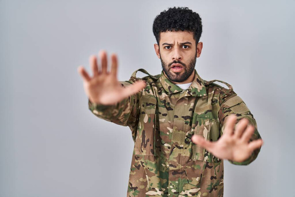 Homme arabe portant un uniforme de camouflage de l'armée faisant geste d'arrêt avec les mains paumes de la main, expression de colère et de frustration  - Photo, image