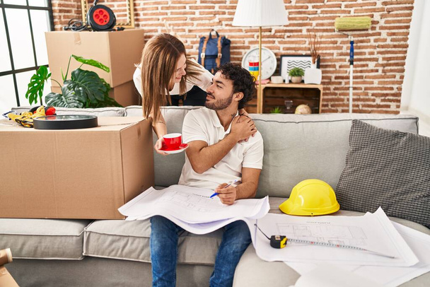 Man and woman couple drinking coffee looking house plans at new home - 写真・画像