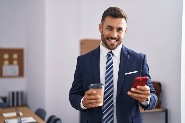Joven trabajador de negocios hispano usando teléfono inteligente tomando café en la oficina - Foto, imagen