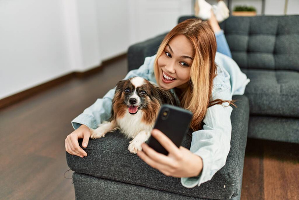 Joven mujer caucásica abrazando perro hacer selfie por teléfono inteligente en casa - Foto, Imagen