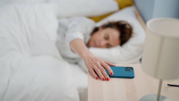 Medioevo donna ispanica spegnere allarme smartphone sdraiato sul letto in camera da letto - Foto, immagini