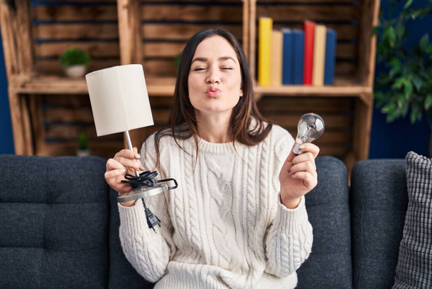 若いブルネットの女性がLED電球とランプを持っていて、カメラを見てキスを吹いて美しいとセクシー。愛の表現.  - 写真・画像