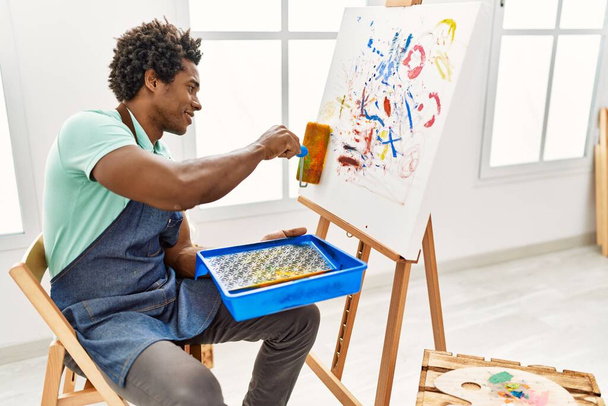 młody afrykański artysta amerykański człowiek rysunek za pomocą rolki farby w studio sztuki. - Zdjęcie, obraz