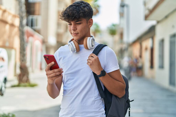 Joven estudiante adolescente hispano sonriendo confiado usando smartphone en la calle - Foto, Imagen