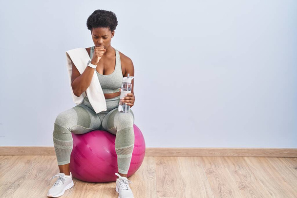 African american woman wearing sportswear sitting on pilates ball feeling unwell and coughing as symptom for cold or bronchitis. health care concept.  - Photo, Image