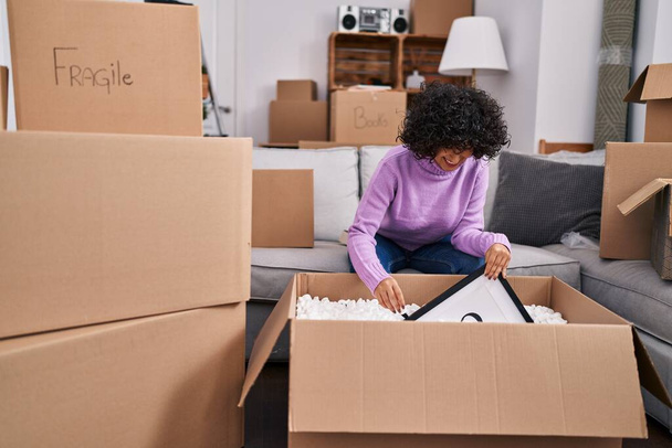 Young middle east woman smiling confident unpacking cardboard box at new home - Foto, Imagen