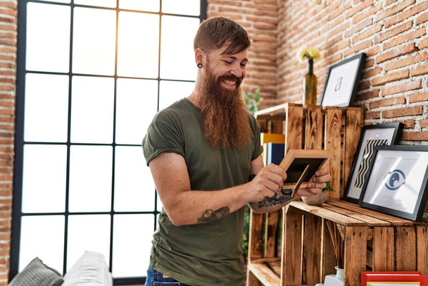 Jeune rousse homme souriant confiant regardant photo à la maison - Photo, image
